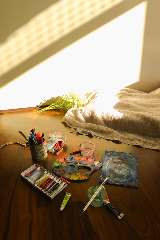 Sunny indoor art setup featuring watercolor paints and brushes on a wooden table.